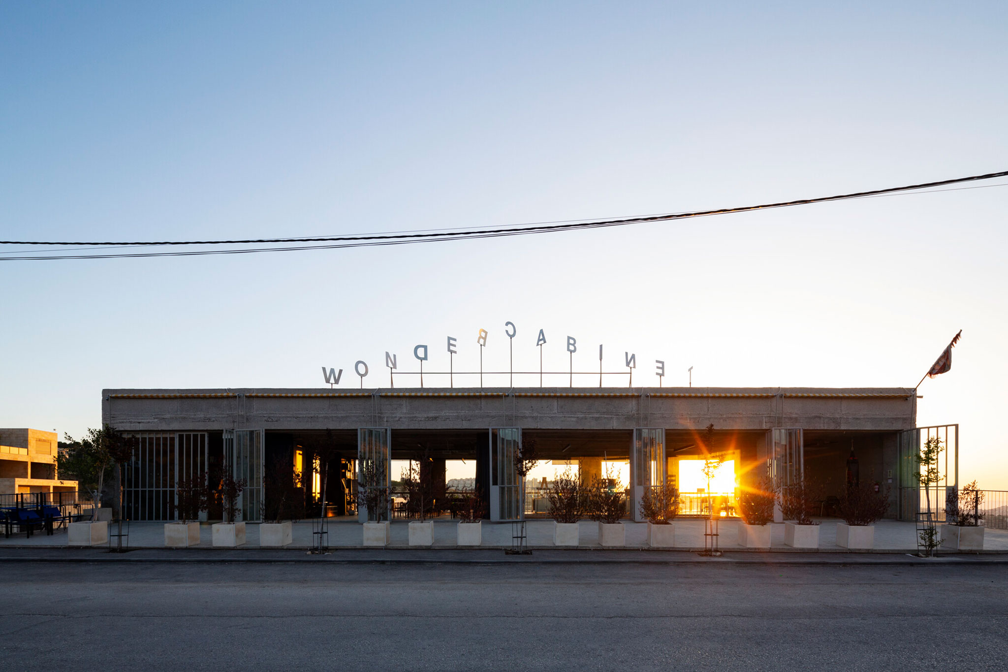 Western facade at sunrise. Decorative elements are minimal, consisting primarily of spinning stainless-steel letters on the roof acting as a weathervane. Aga Khan Trust for Culture / Mikaela Burstow.