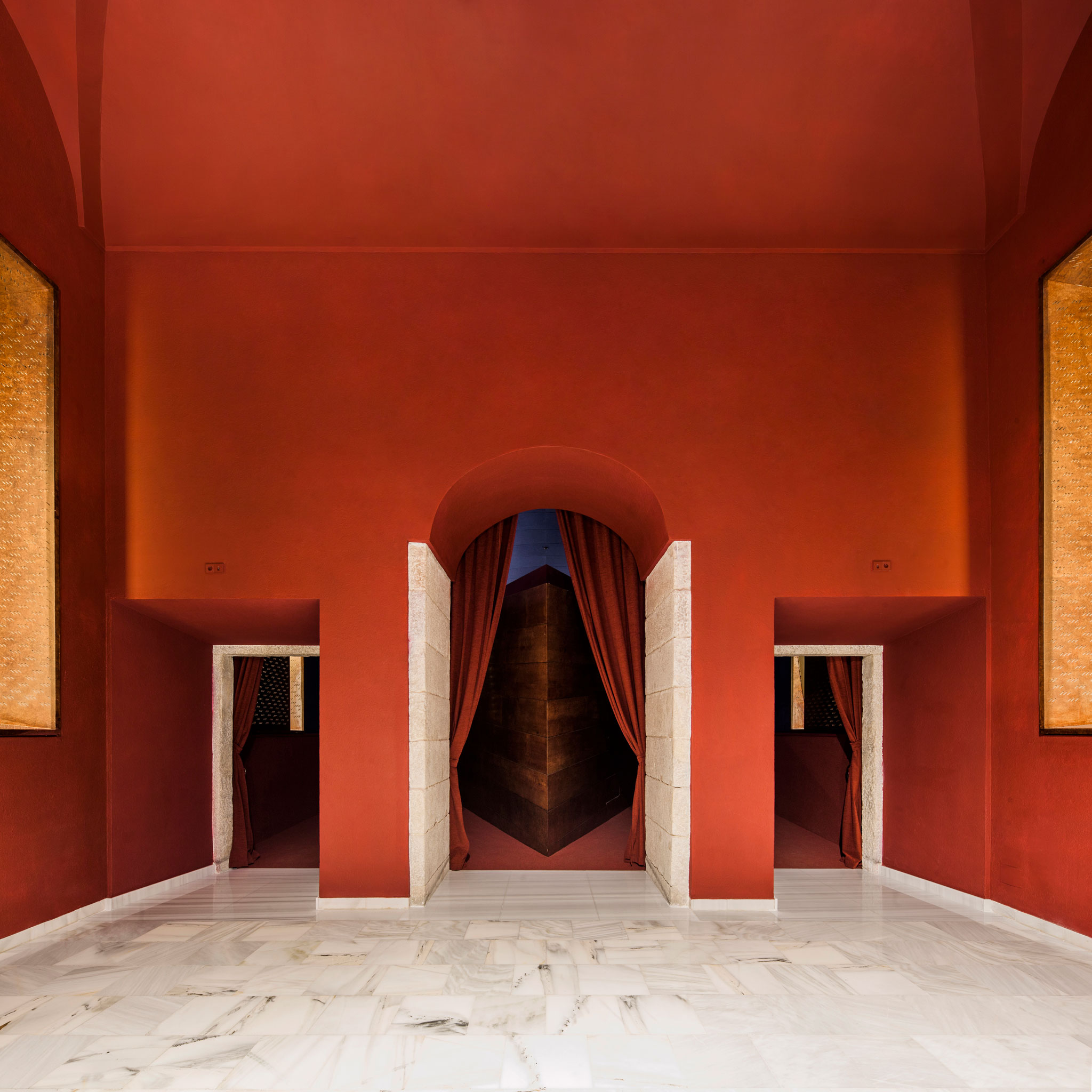 BACH / Jaume Bach + Anna & Eugeni Bach maintain the dialogue between the original vaulted space and the abstract geometry proposed in 1987, designing a renovation that maintains the iconic elements of that proposal: the small triangular projection room that organizes and divides the circulation at the entrance, and the triangle suspended above the stage, which functioned as a reverberation device and now serves as an acoustic screen that conceals the center speakers. To adapt to current programmatic and technical image and sound requirements, the translation booths have been eliminated, and the slope of the stalls' floor has been modified to improve screen visibility. The windows are closed with carved wooden panels, and the Serliana is preserved in a unique shade of red that welcomes visitors. Inside, the furniture has been renovated to improve the visibility of the film set, and the iconic suspended triangle has been transformed into a large acoustic screen that conceals its center speakers.