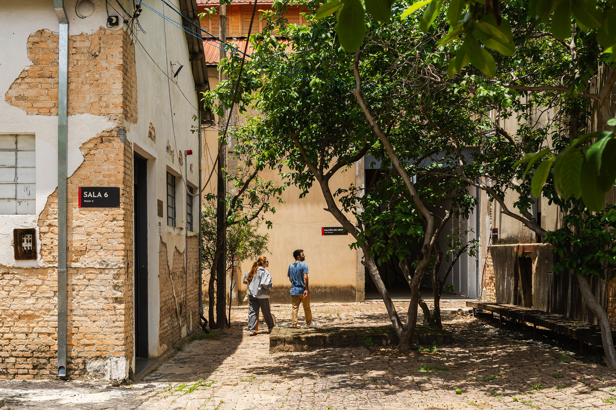 Vista de la esquina entre el Atelier Residencial I, el Edificio de Exposiciones J y el Atelier K, mostrando diferentes enfoques de renovación dentro de un ambiente verde. Fábrica de Arte Marcos Amaro (FAMA) por KAAN. Fotografía de Sebastian van Damme.