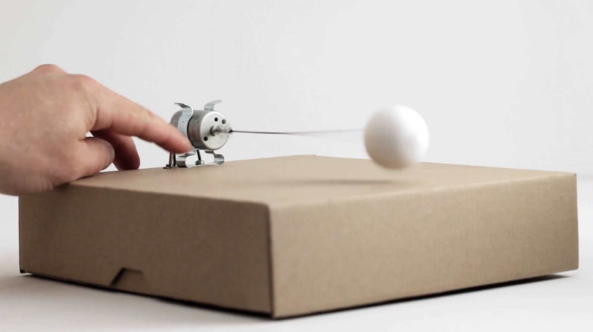 Video screenshot. 1 prepared dc-motor, cotton ball, cardboard box 23x23x6cm by Zimoun