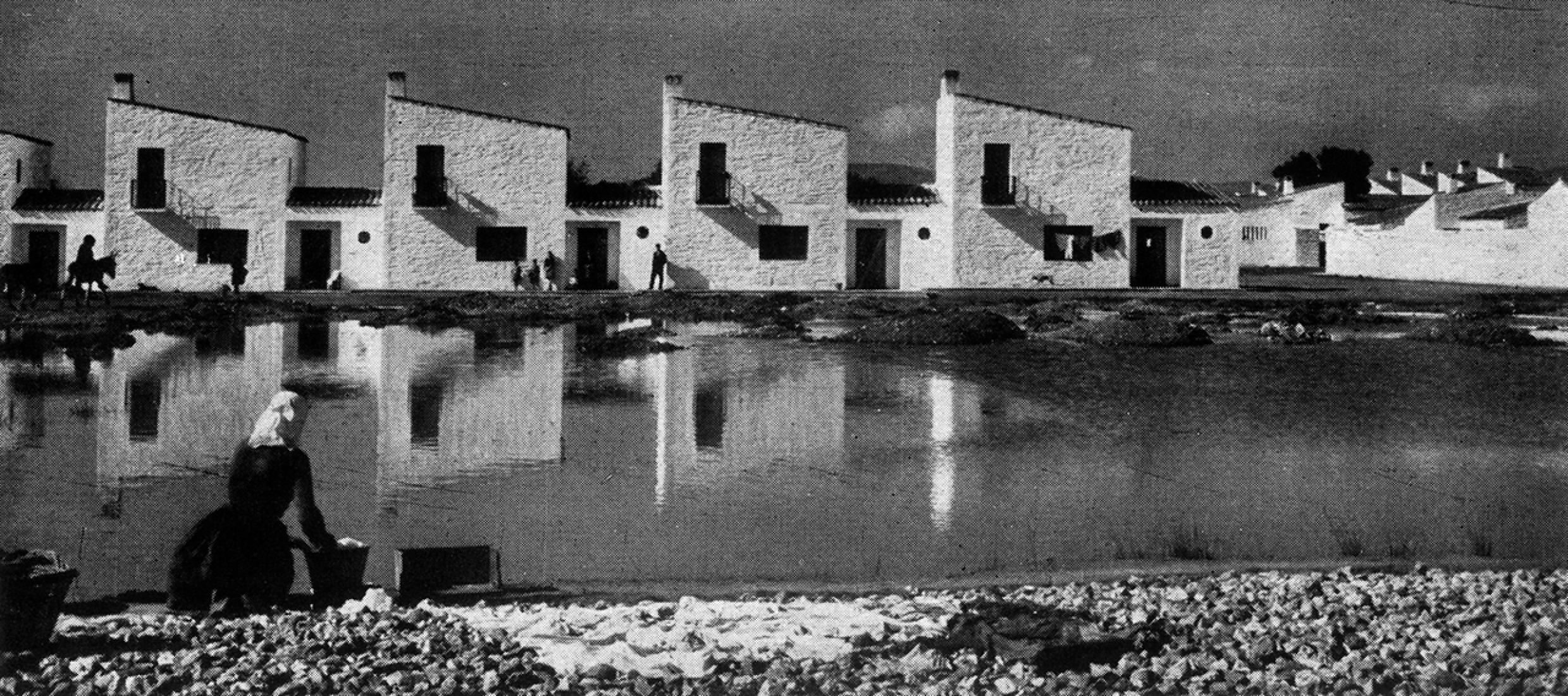 Imagen canónica de Vegaviana, con la lavandera delante de un grupo de casas seriadas, por Kindel; de F.J. Sáenz de Oíza: «El pueblo de Vegaviana. Cáceres. José Luís Fernández del Amo», Arquitectura, n.7, Madrid: Colegio Oficial de Arquitectos de Madrid, julio 1959, (pp.25-28) p.25.