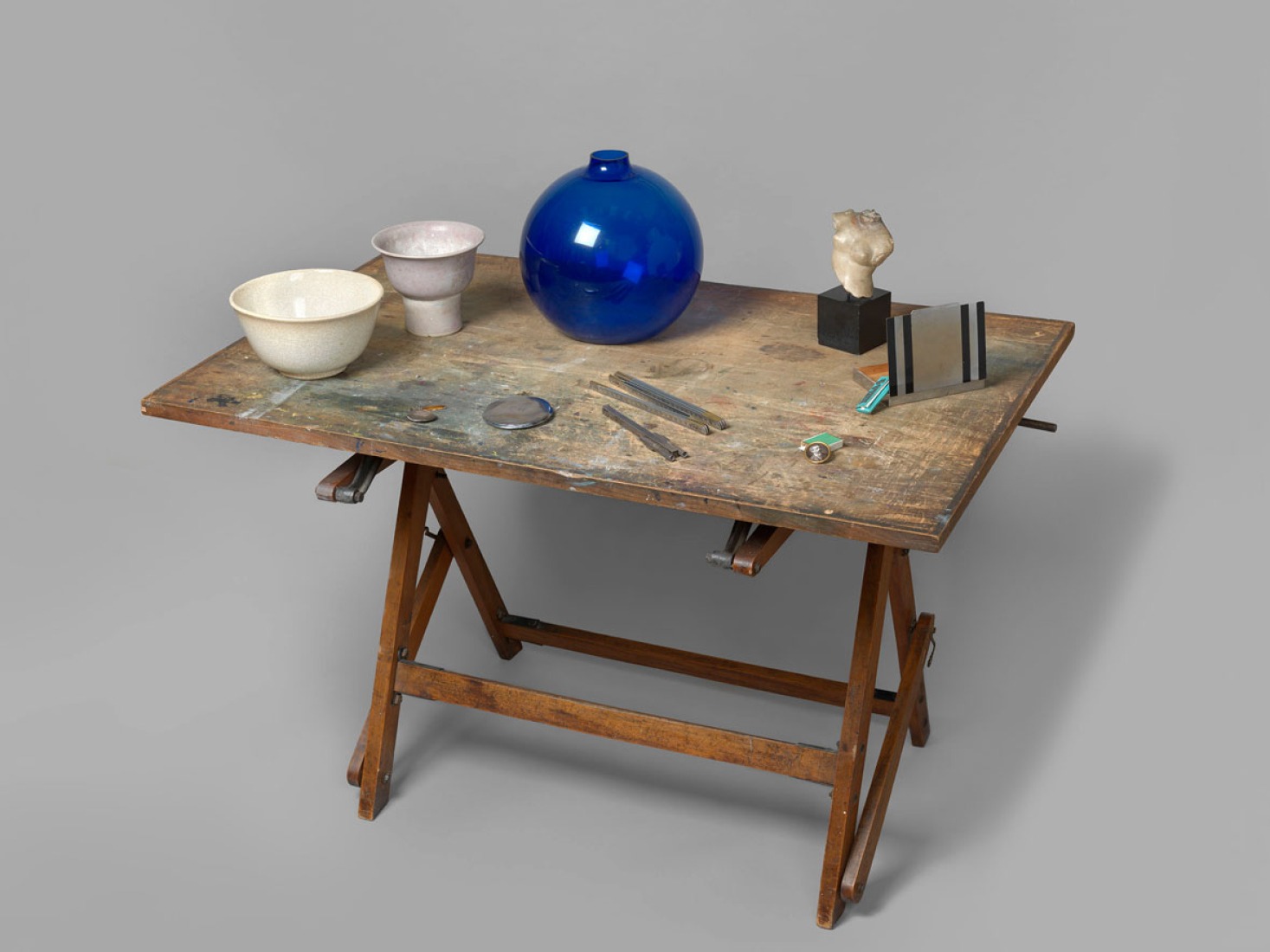 Mesa con florero de cristal azul,concha con soporte, escultura africana con base lacada, torso griego sobre base de mármol, dos cuencos de cerámica y un pequeño caballete de madera. Exposición Eileen Gray: la pintora privada. Imagen cortesía de la Osborne Samuel Gallery. 