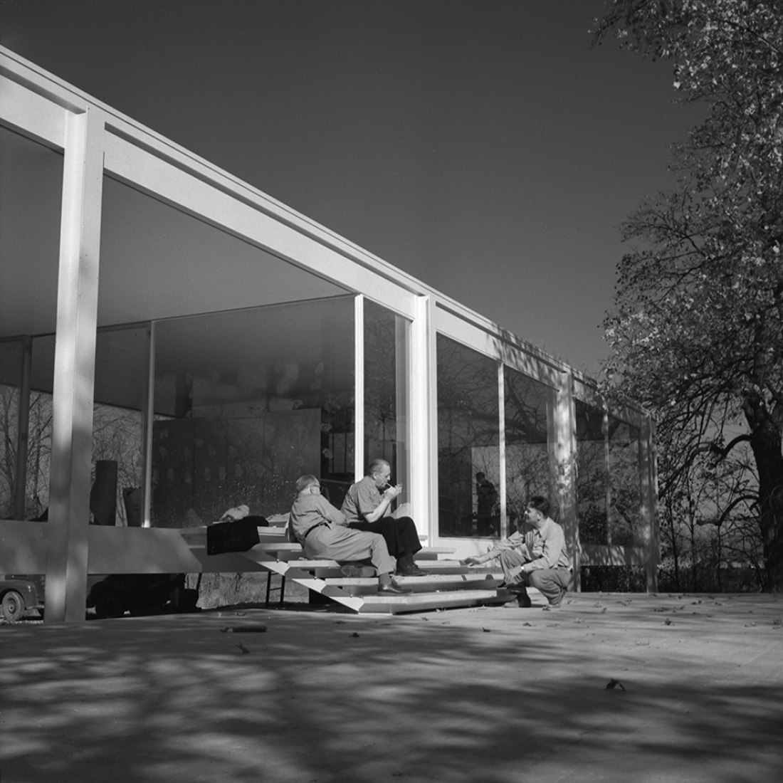 Foto de Mies sentado en las escaleras sobre la plataforma de la casa Farnsworth encendiendo un puro