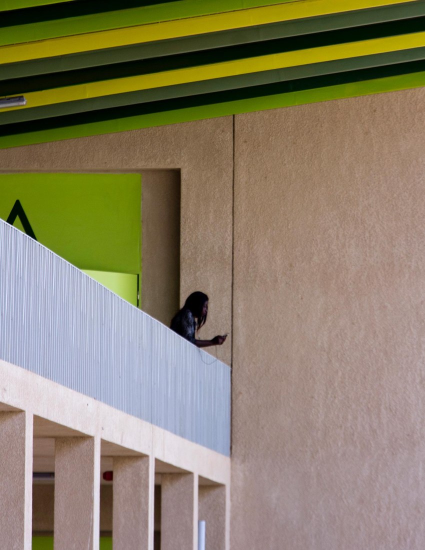 Mujer joven apoyada contra la barandilla del pasillo exterior. Nuevo edificio Aulario en la universidad Alioune Diop por IDOM. Fotografía por Aga Khan Trust for Culture / Chérif Tall (photographer)