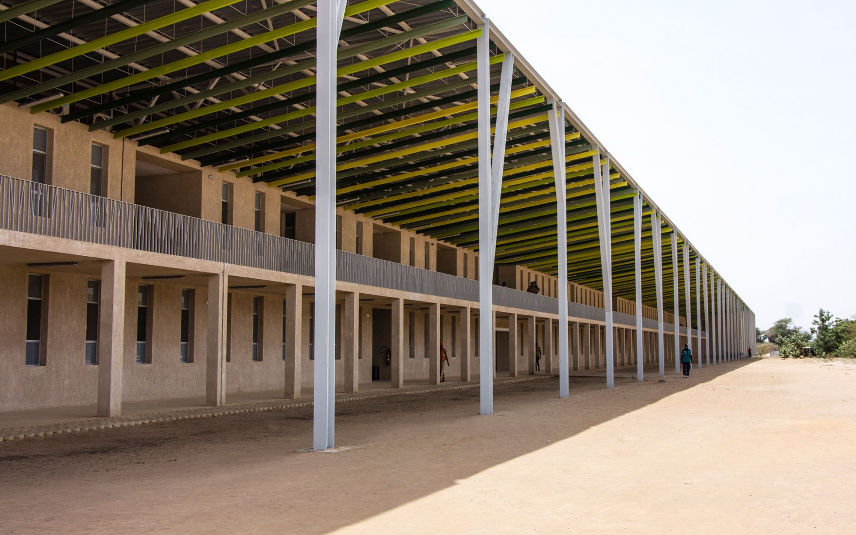 La estructura de la cubierta está pensada como un gran árbol que protege la vida debajo de él y crea un espacio público de usos múltiples. La forma de las columnas de techo volador emula el tronco de un árbol y sus ramas. Marca fuertemente la identidad del proyecto como un todo. Nuevo edificio Aulario en la universidad Alioune Diop por IDOM. Fotografía por Aga Khan Trust for Culture / Chérif Tall (photographer)