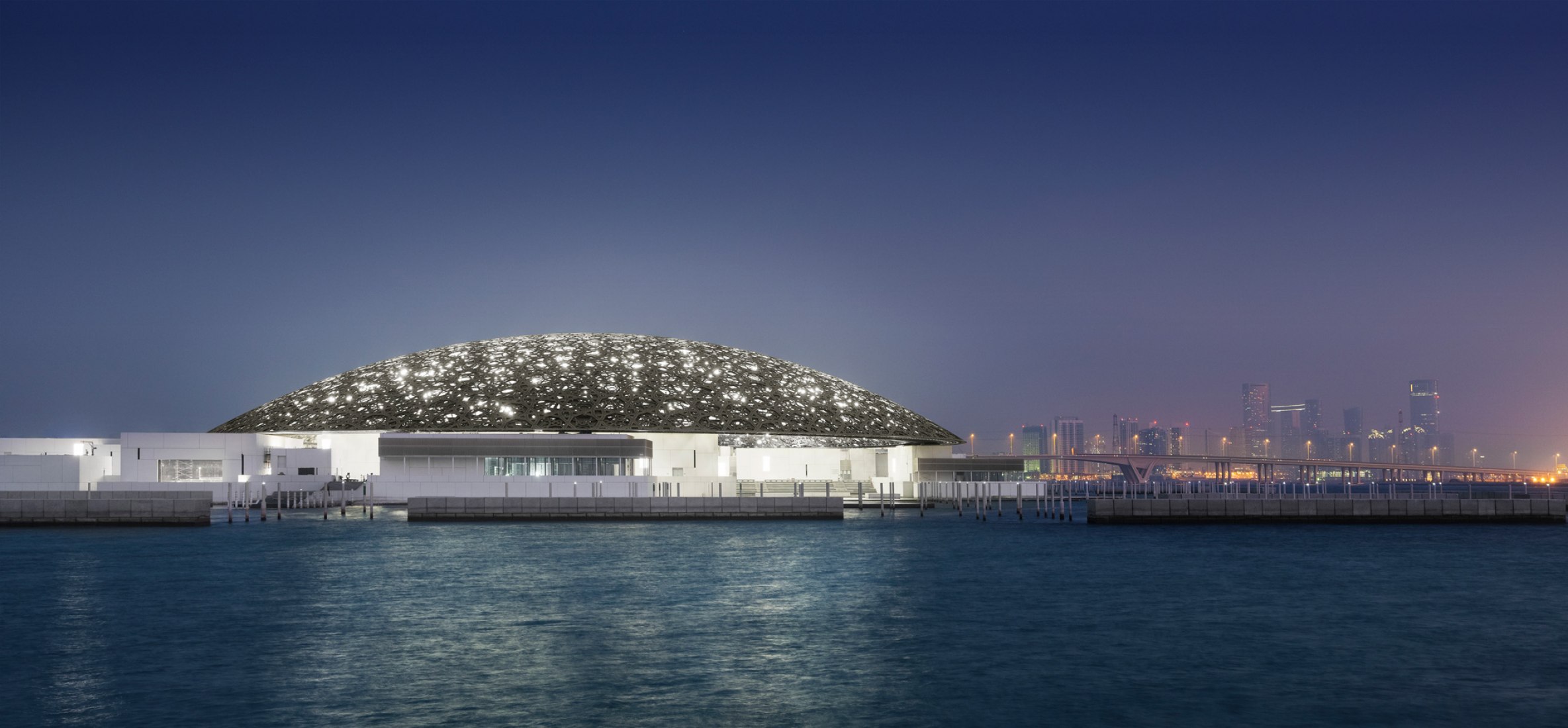 Vista exterior nocturna con el perfil de Abu Dhabiís. Louvre Abu Dhabiís por Jean Nouvel. Fotografía  © Louvre Abu Dhabi, Fotografía.- Mohamed Somji