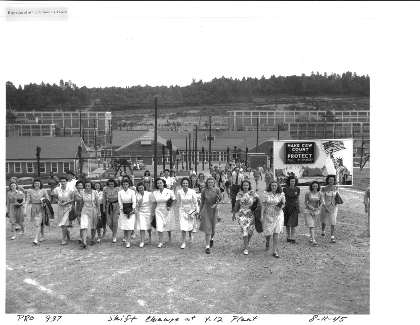 Shift change at the Y-12 plant, Oak Ridge, 1945. Many of the workers in the three Secret Cities of the Manhattan Project were young women. The group seen here is leaving the Y-12 plant, where uranium was enriched through electromagnetic separation. The sign in the right background says “Make C.E.W. count.” C.E.W. was the abbreviation for the Clinton Engineer Works, the official name of the Oak Ridge industrial site during the war, derived from the nearby town of Clinton, TN. Courtesy of the U.S. Department 